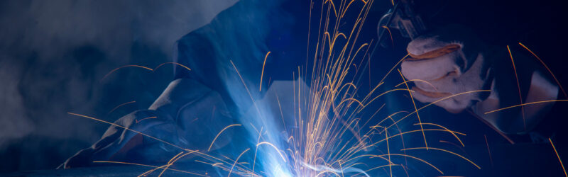 Professional welder and mask welding metal pipe on the industrial table.